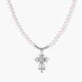 White pearl necklace with ornate silver cross pendant featuring zirconia crystals on cream background.