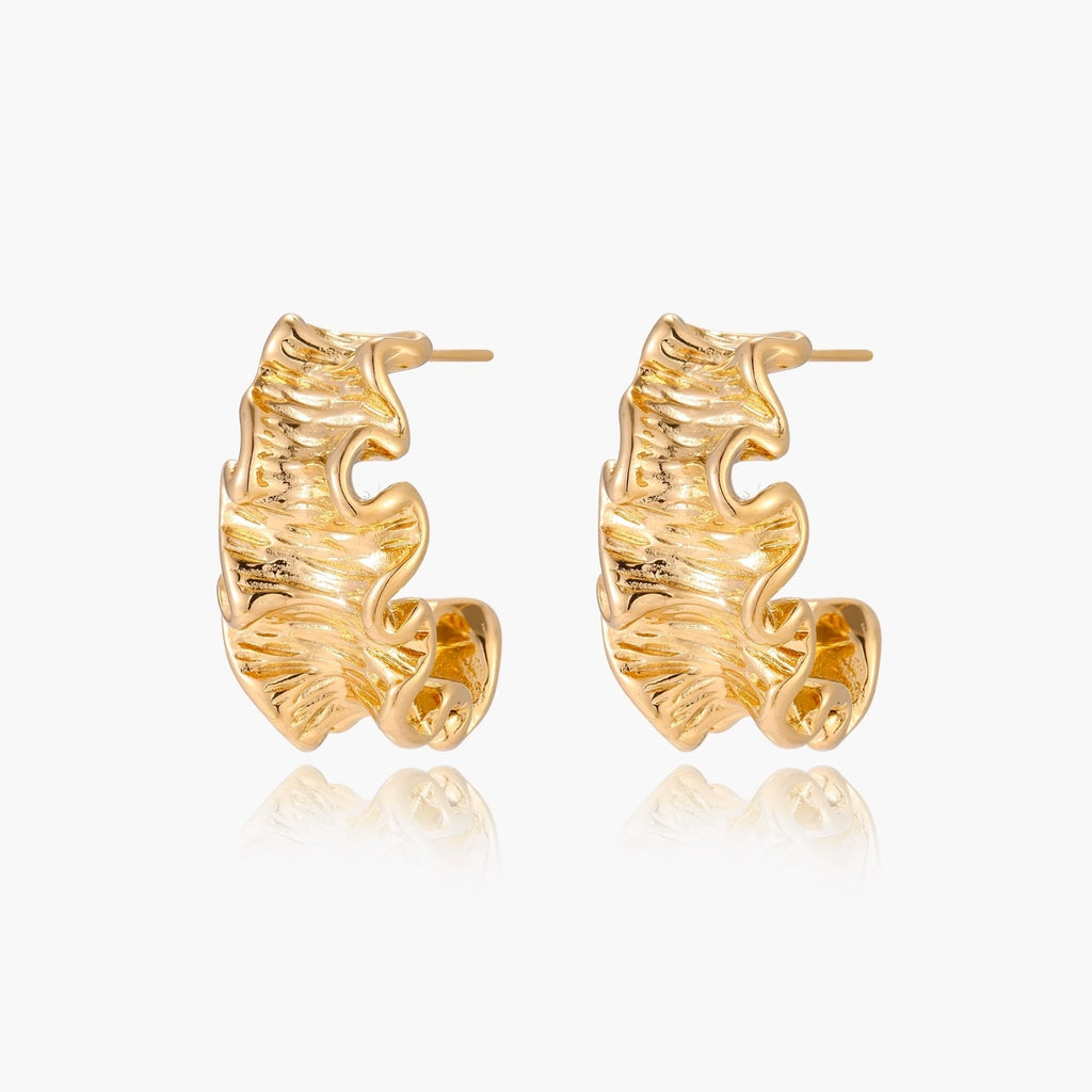 Pair of gold huggie hoops with sculpted wave texture and dimensional ripples on neutral background.