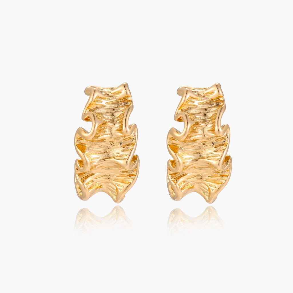 Pair of gold huggie hoops with sculpted wave texture and dimensional ripples on neutral background.