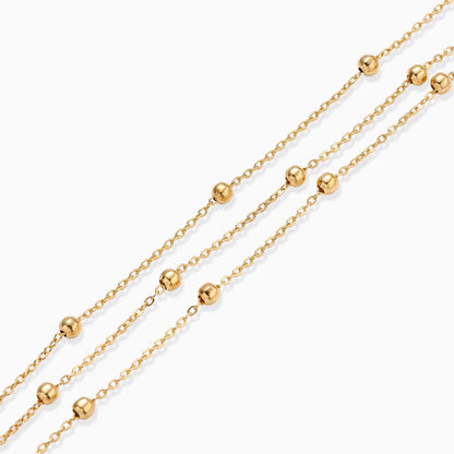 Three-strand gold-plated bracelet with clustered ball beads and adjustable clasp on cream background