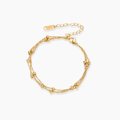 Three-strand gold-plated bracelet with clustered ball beads and adjustable clasp on cream background