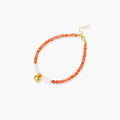 Beaded bracelet with coral-orange carnelian stones, white pearls, and gold heart charm on cream background